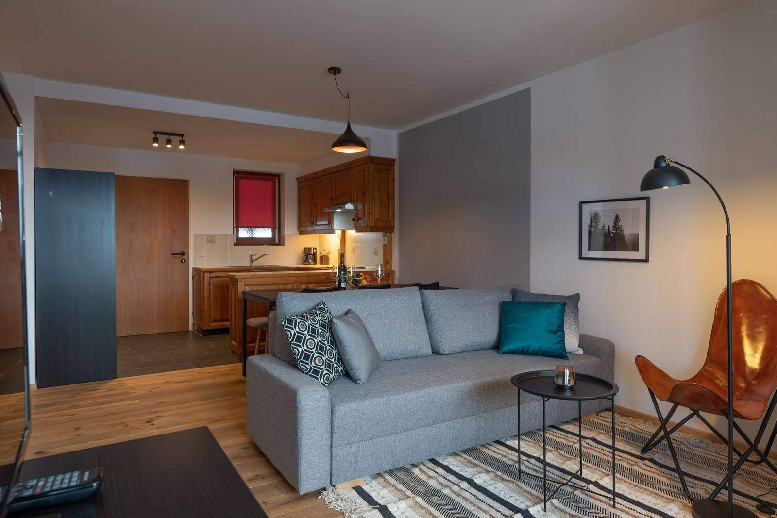 Helles Wohnzimmer mit Sofa, Ledersessel und Küche – Ferienwohnung auf der Gerlitzen Alpe